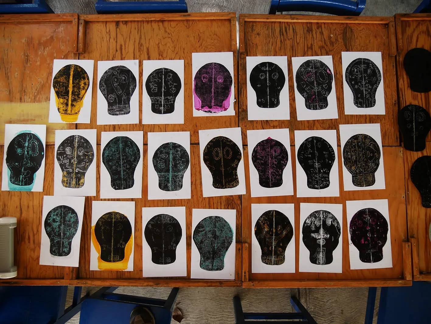 Una hilera de impresiones de cráneos, en negro con detalles de colores, secándose sobre la mesa.