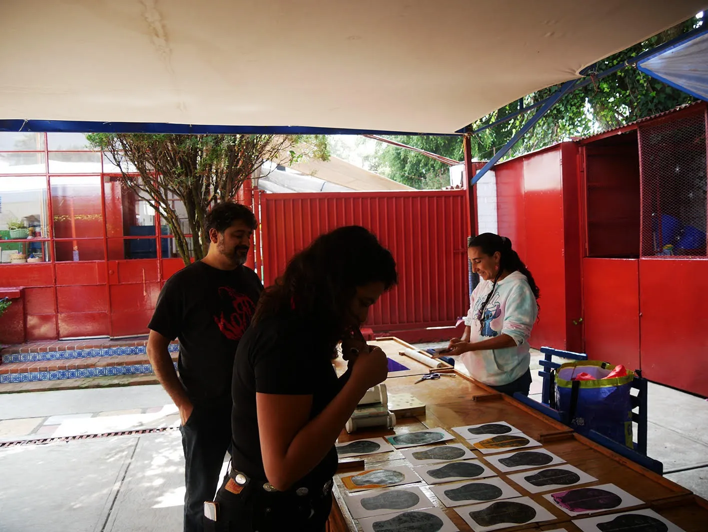 Dos personas conversan junto a la mesa de estampado, bajo el toldo del patio.