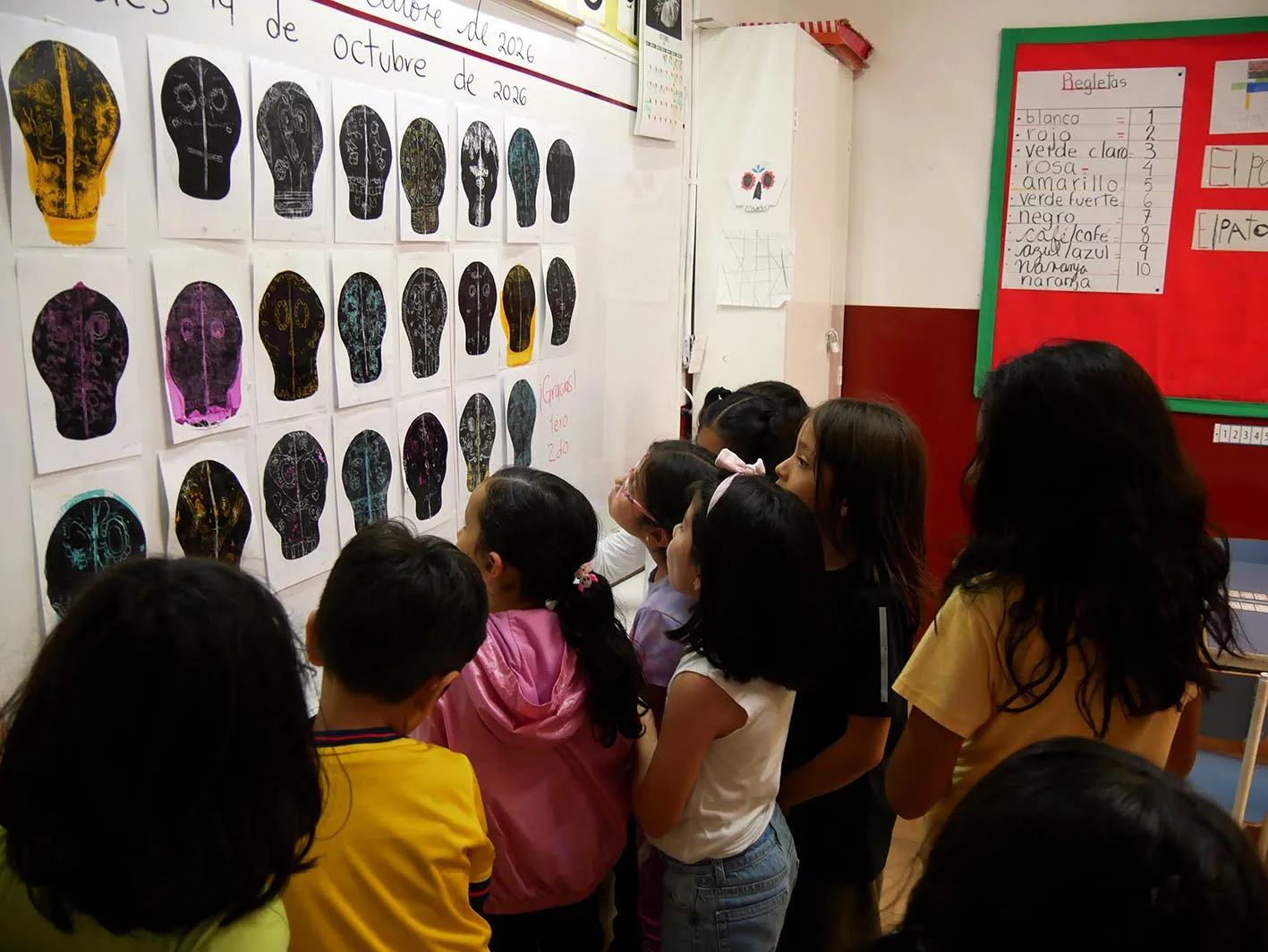Niñas y niños miran el muro de cráneos impresos que cuelga en el salón.