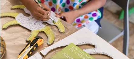 Manos de niñas y niños que recortan y pegan papeles de colores sobre una mesa.